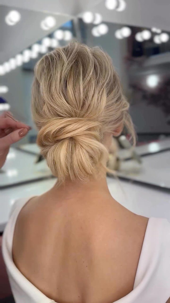 18 Low Messy Bun for Wedding Ideas with Braids and Florals 7 Blonde hair styled in a voluminous twisted low chignon bun from behind.
