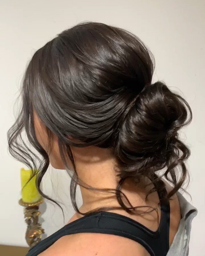 18 Low Messy Bun for Wedding Ideas with Braids and Florals 17 Low messy bun hairstyle on dark brown hair with loose curling tendrils.