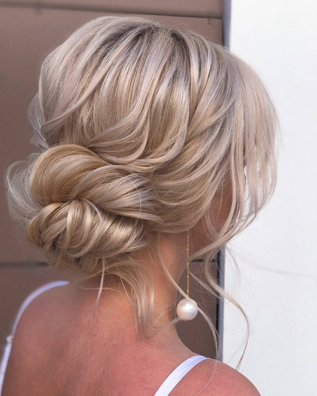 18 Low Messy Bun for Wedding Ideas with Braids and Florals 12 Blonde hair styled in a low messy bun with a single pearl earring.