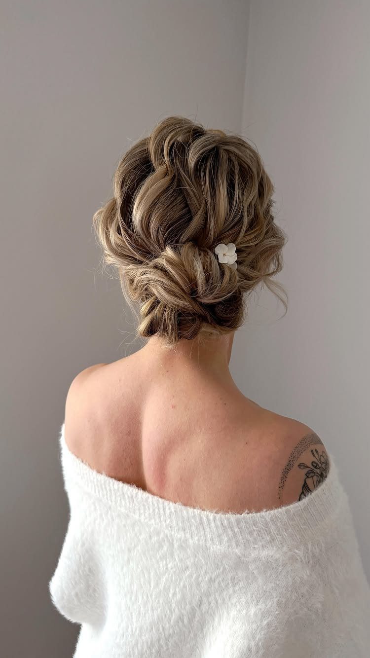 18 Low Messy Bun for Wedding Ideas with Braids and Florals 3 Blonde woman from behind with a soft elegant low bun and white sweater.
