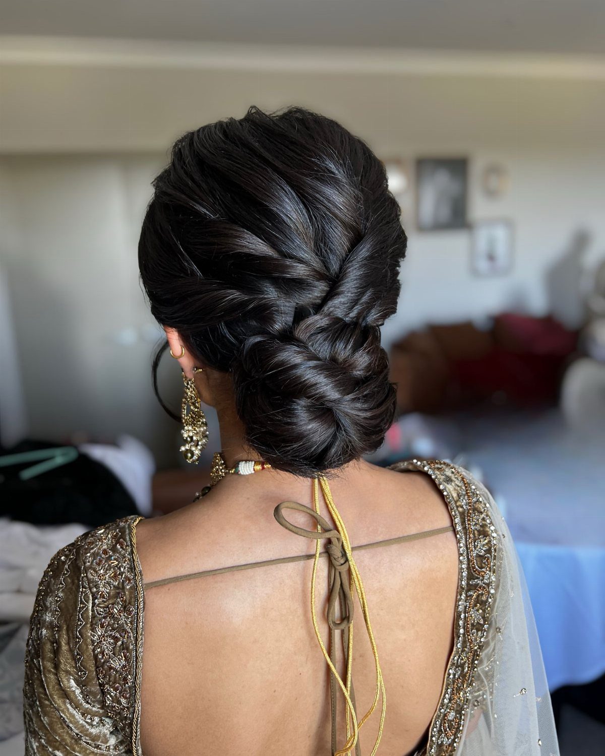 18 Low Messy Bun for Wedding Ideas with Braids and Florals 8 Twisted low bun hairstyle on a person wearing gold bridal attire and jewelry.