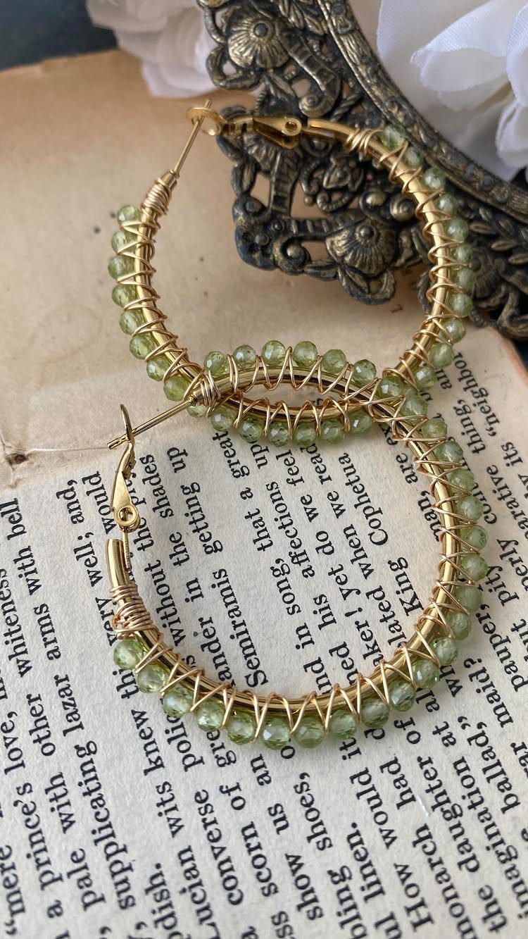 Gold wire hoop earrings wrapped with small translucent green beads resting on an open book.