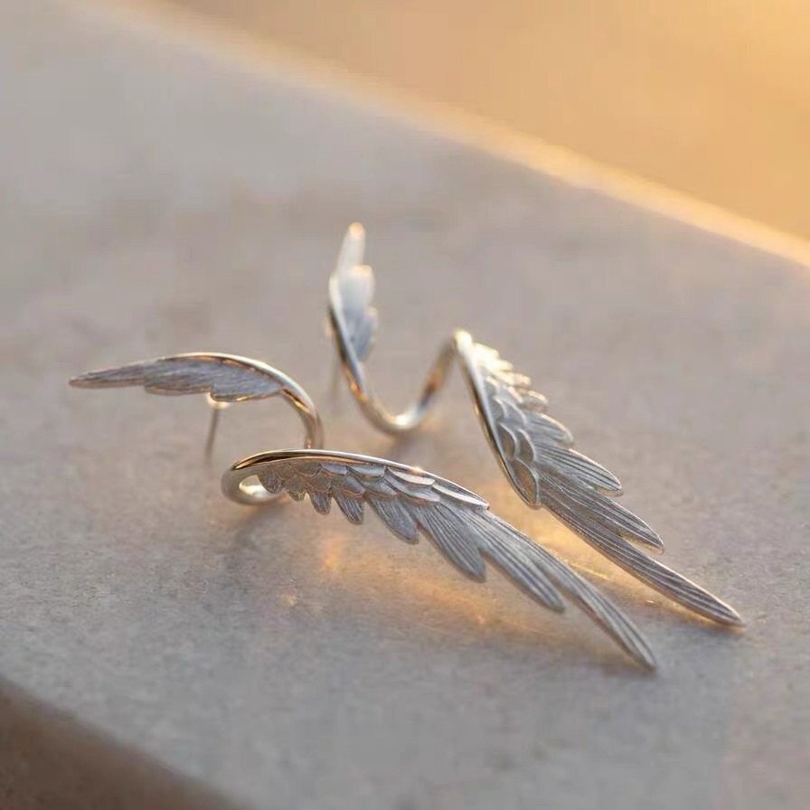 Silver wing-shaped earrings with detailed feather textures resting on a light stone surface.