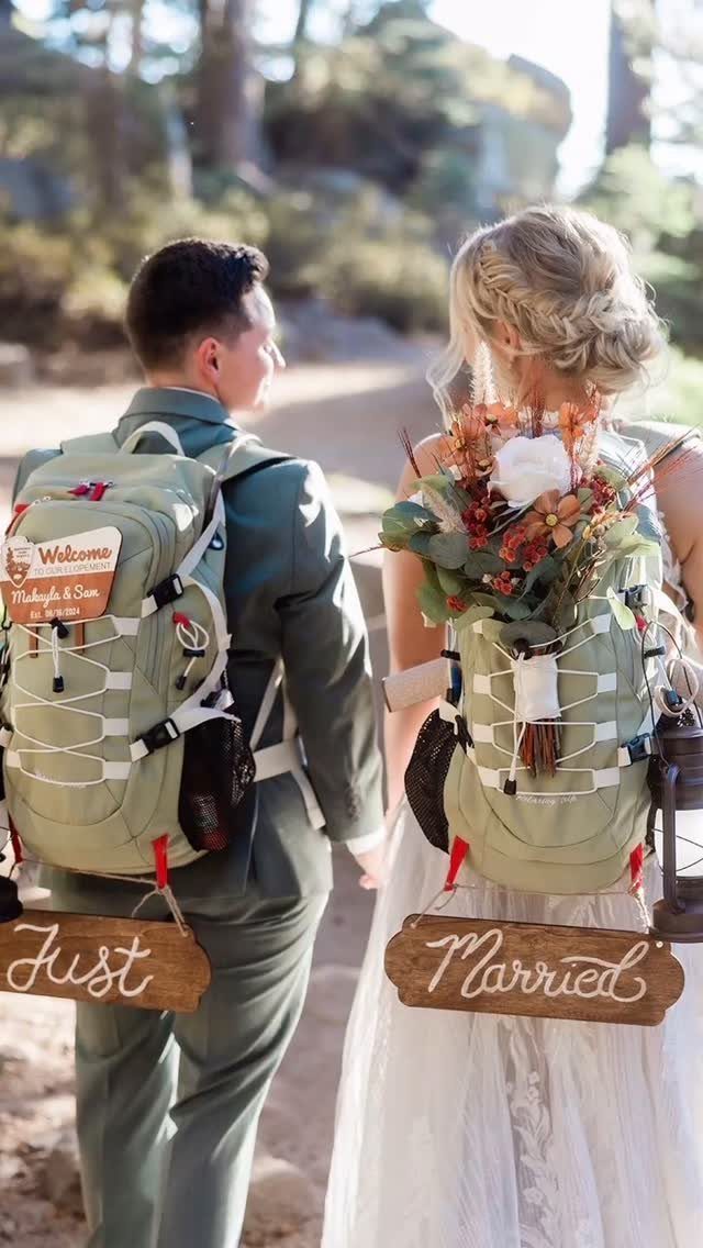 19 Mountain Wedding Ideas for Scenic, Cozy Celebrations 9 Bride and groom wearing hiking backpacks with Just Married signs walking through a forest.