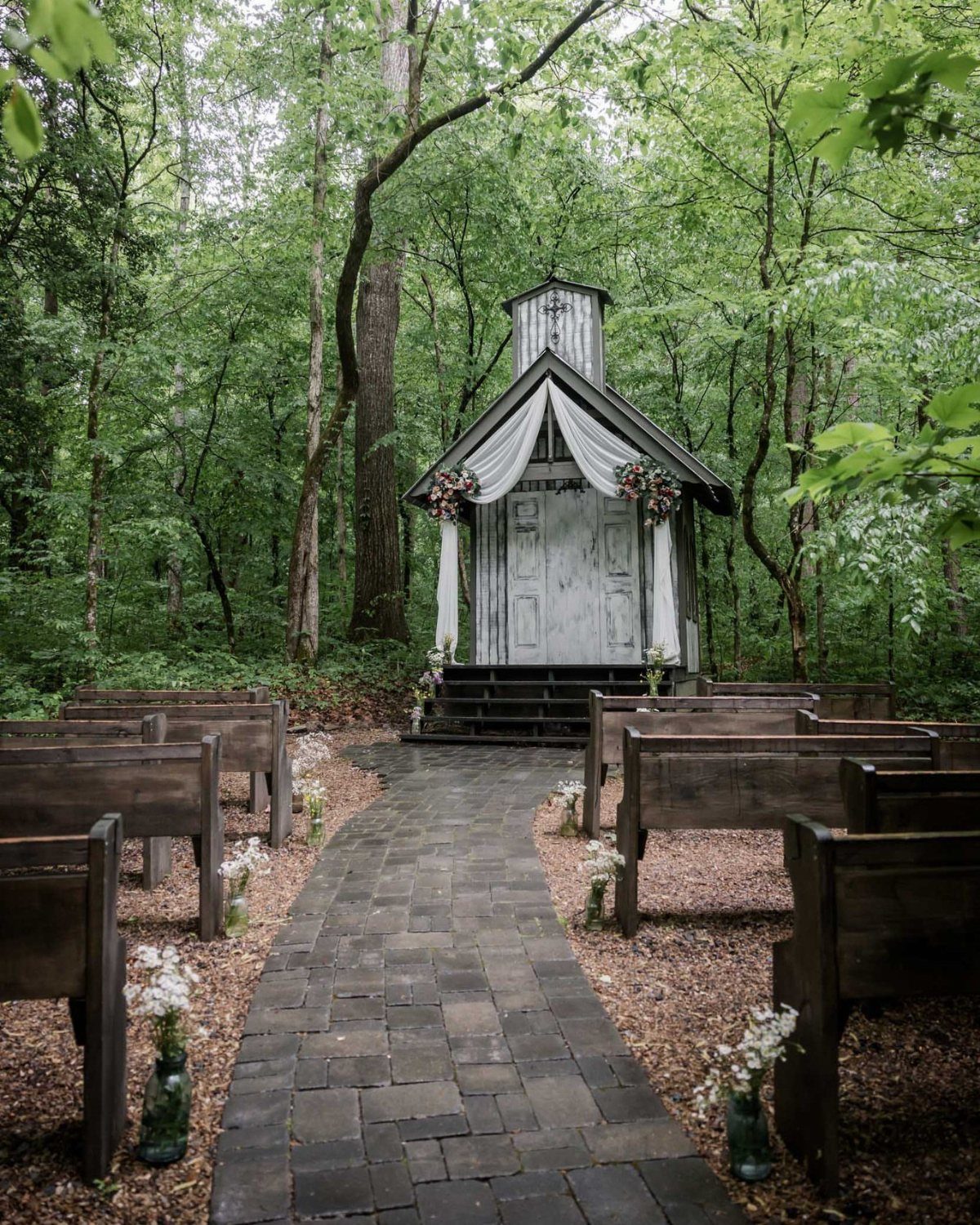 19 Mountain Wedding Ideas for Scenic, Cozy Celebrations 11 Wooden chapel in a green forest with a stone path and wooden pews.