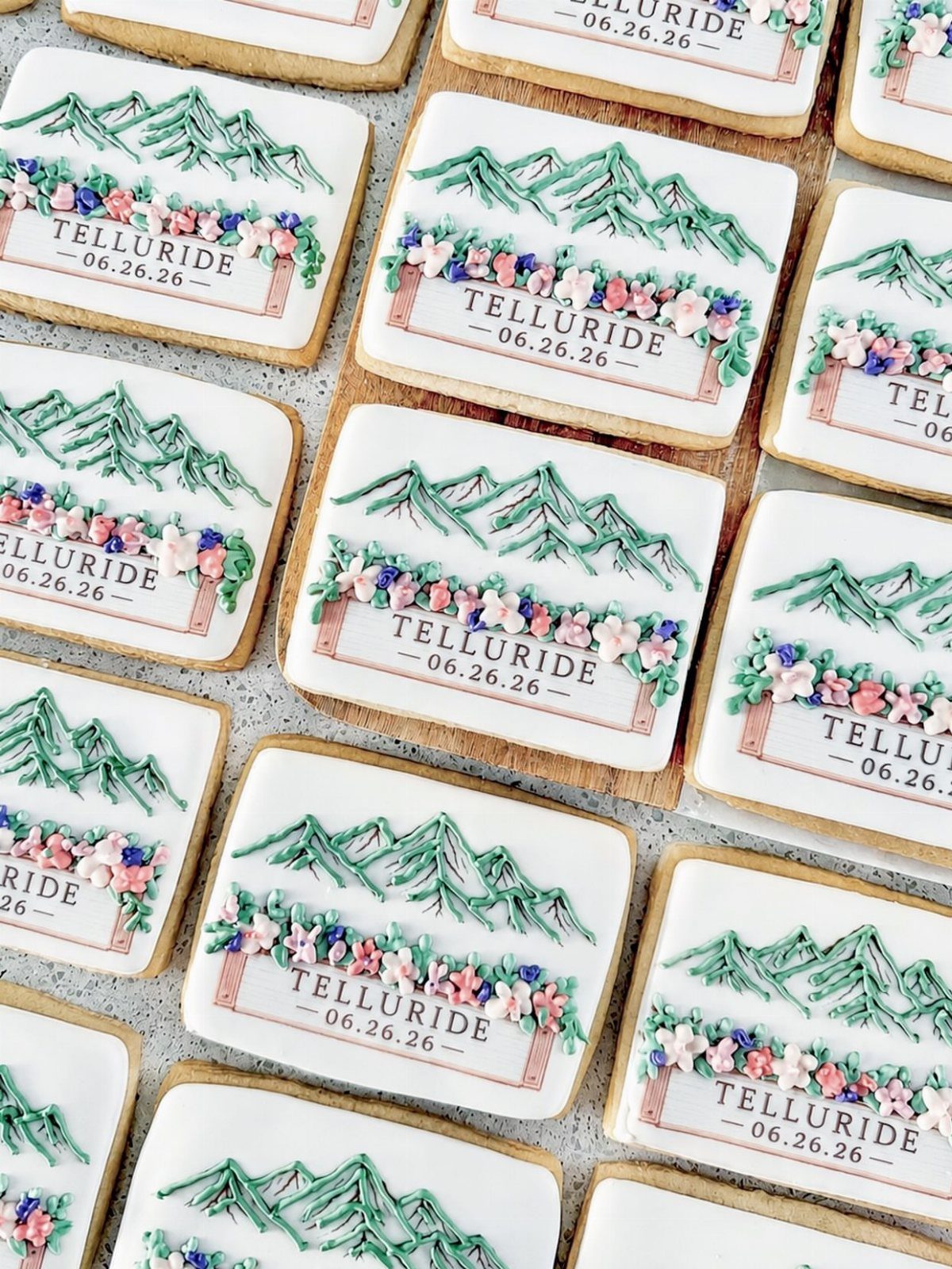 19 Mountain Wedding Ideas for Scenic, Cozy Celebrations 19 Custom sugar cookies decorated with green mountains, flowers, and Telluride wedding date text.