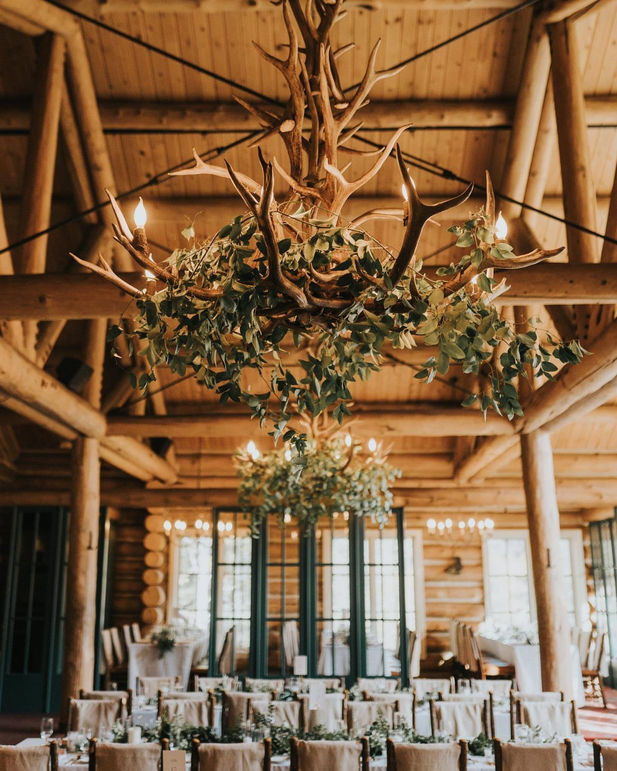 19 Mountain Wedding Ideas for Scenic, Cozy Celebrations 12 Rustic log cabin reception hall with antler chandeliers and elegantly set dining tables.