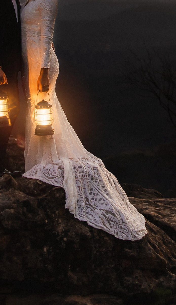 19 Mountain Wedding Ideas for Scenic, Cozy Celebrations 20 Bride in lace wedding dress holding a glowing lantern on a dark rocky cliff