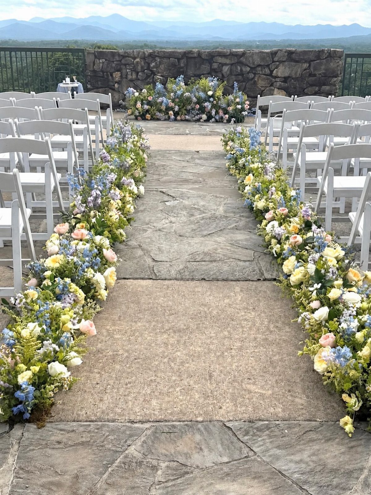 19 Mountain Wedding Ideas for Scenic, Cozy Celebrations 3 Wedding aisle lined with blue and yellow floral arrangements overlooking distant blue mountains.