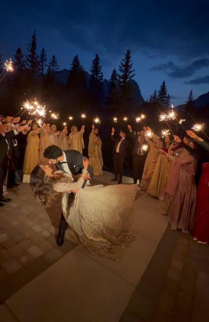 19 Mountain Wedding Ideas for Scenic, Cozy Celebrations 10 Bride and groom kissing while guests hold sparklers against a mountain backdrop at dusk