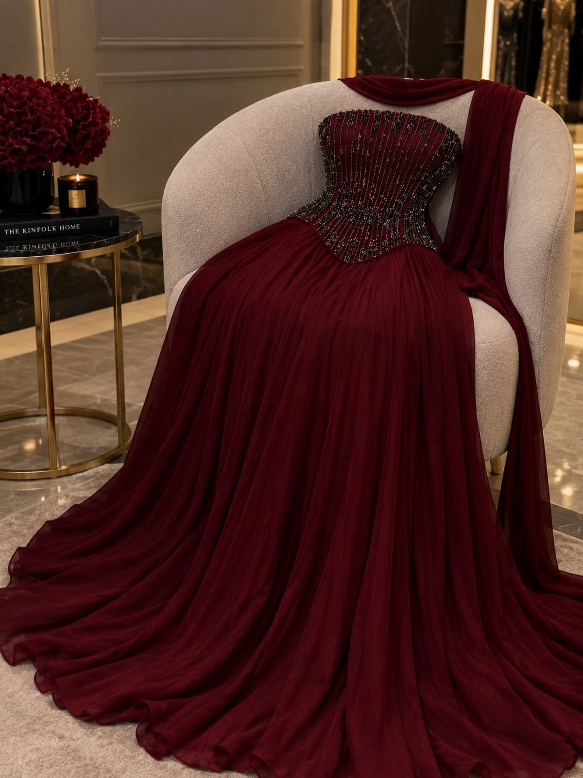 Burgundy chiffon gown with beaded bodice and side cape draped over a grey chair.