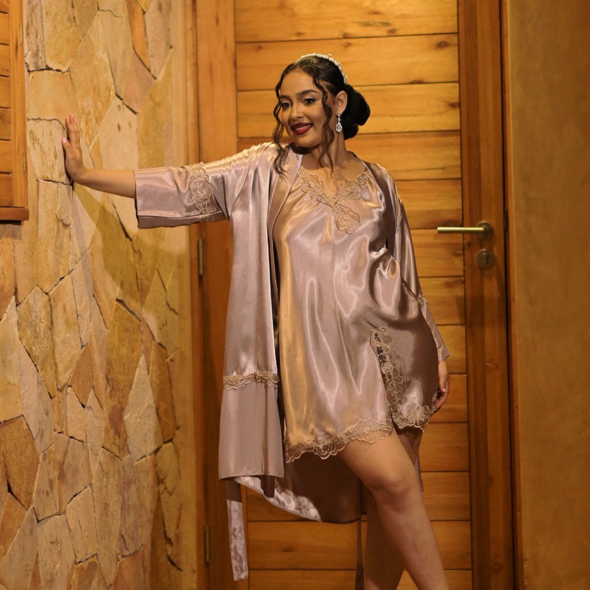 Woman in champagne satin nightdress and robe posing by a stone wall