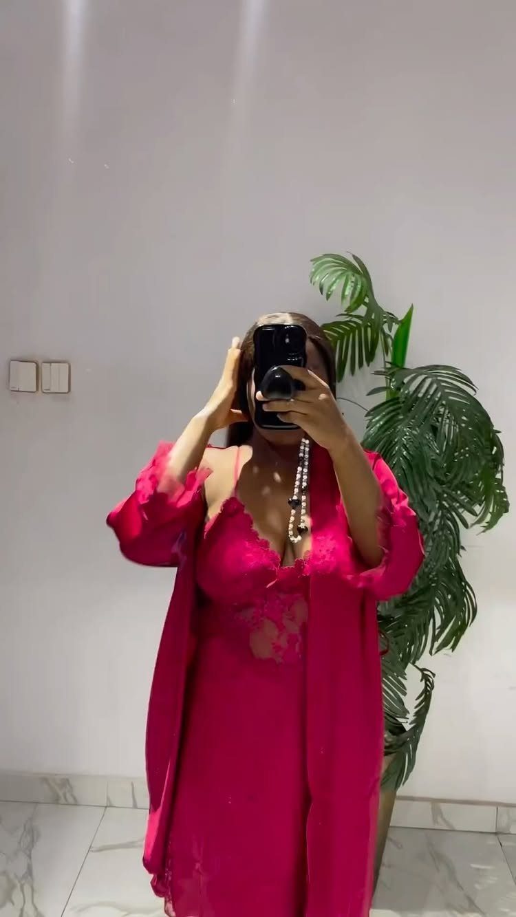 Woman in pink lace nightdress and matching robe taking a mirror selfie.