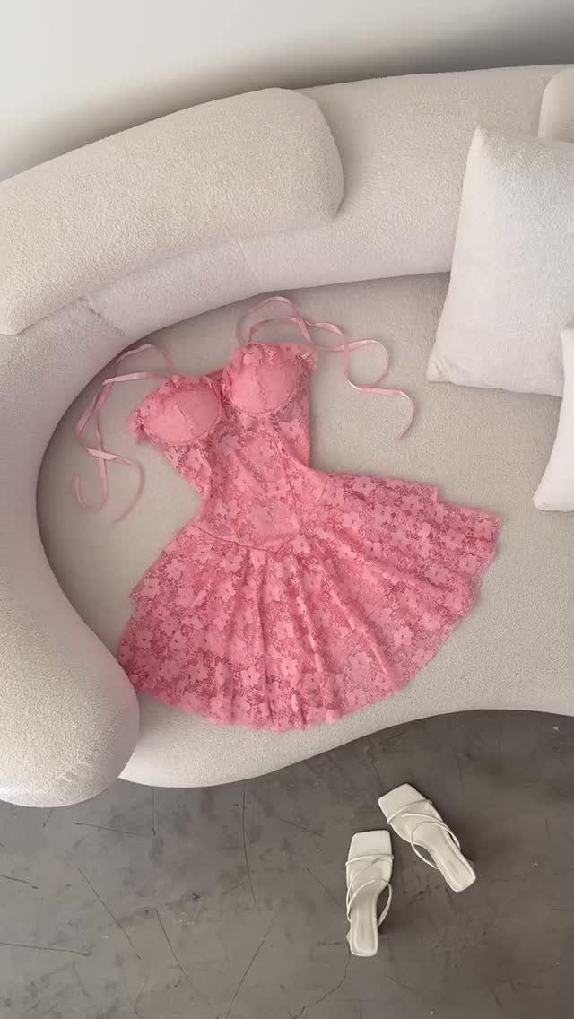 Pink lace babydoll nightdress laid on a white curved boucle sofa with white sandals.