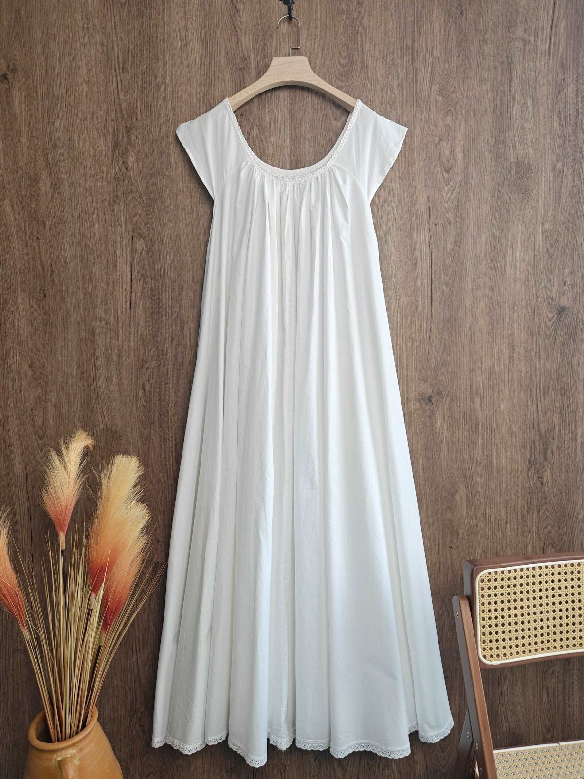 White cotton nightdress hanging on a wooden hanger against a wood-paneled wall.