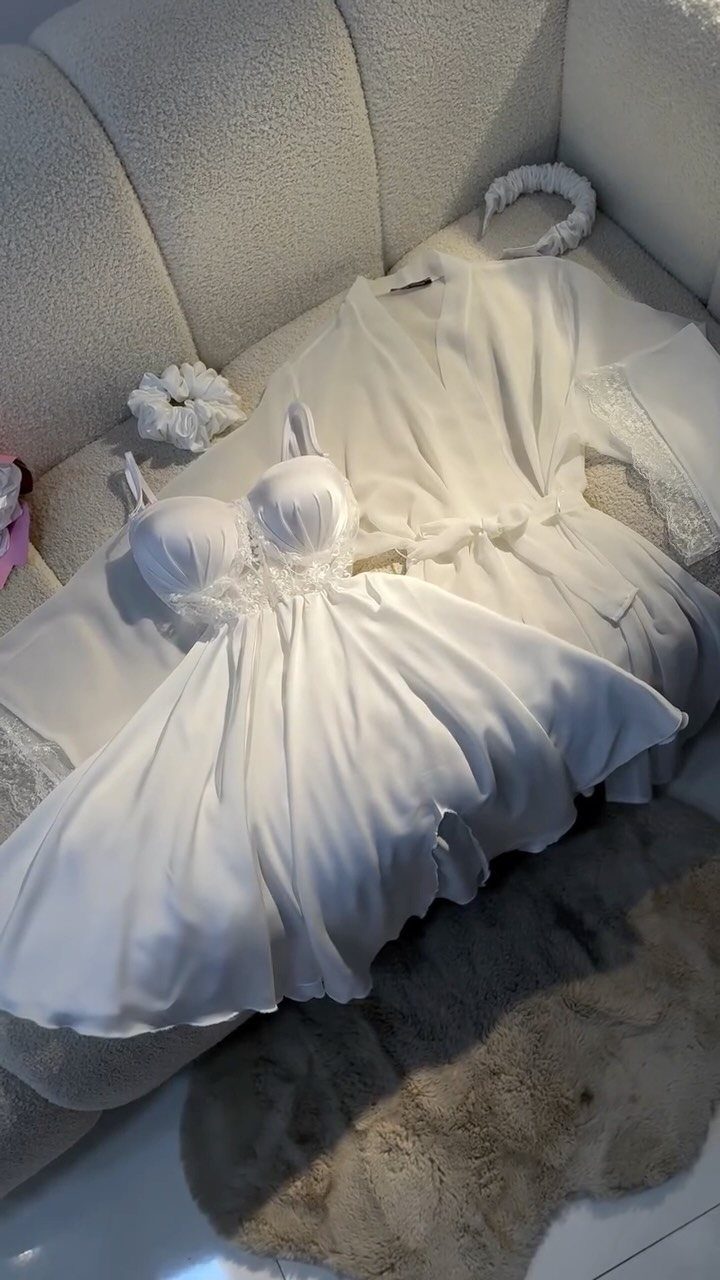 White satin short nightdress and matching robe laid on a white textured sofa.