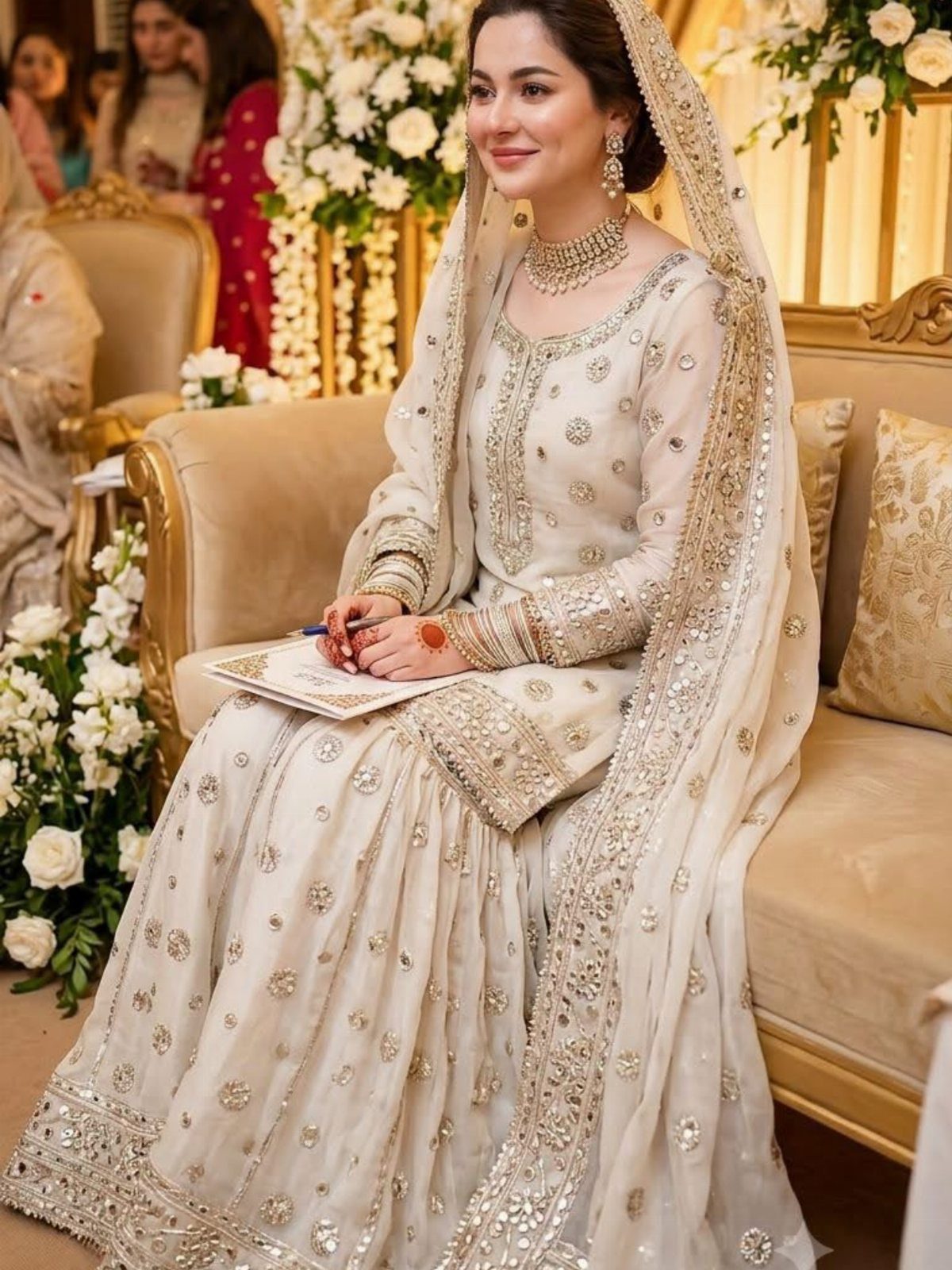26 Nikah Dress Ideas for Your Perfect Wedding Ceremony 12 Woman in an embellished ivory Anarkali dress and dupatta sitting on a sofa.