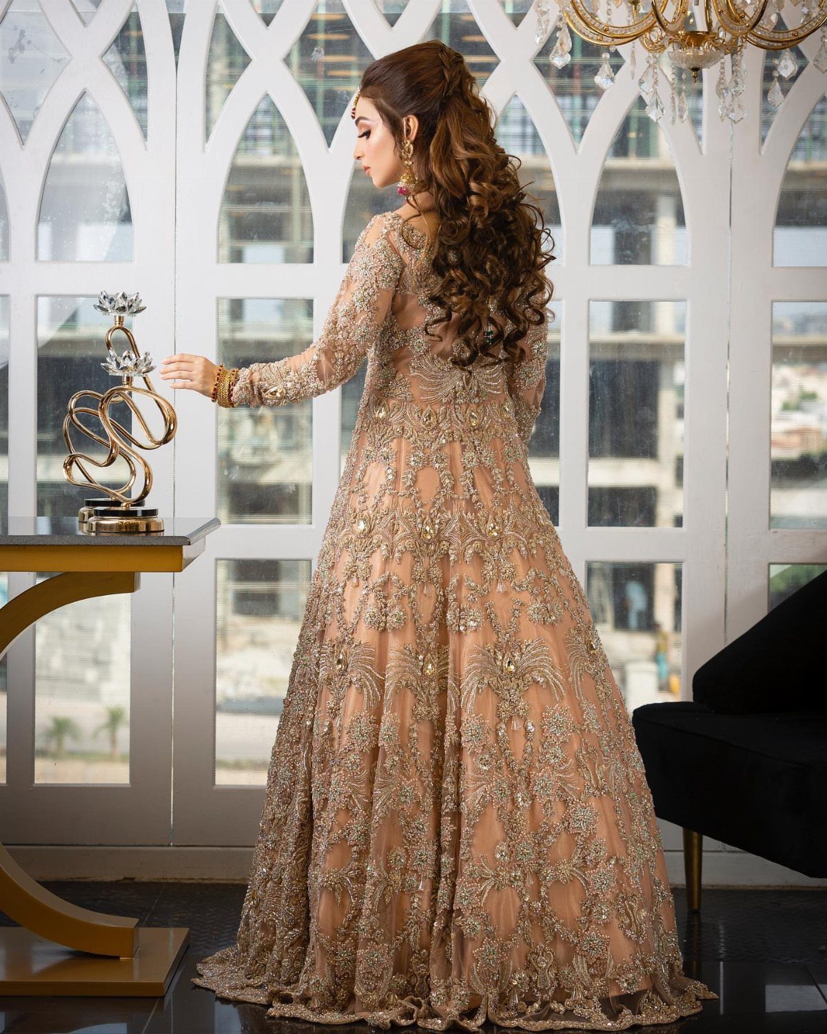 26 Nikah Dress Ideas for Your Perfect Wedding Ceremony 25 Woman in a soft peach gown with gold floral embroidery standing by a window.