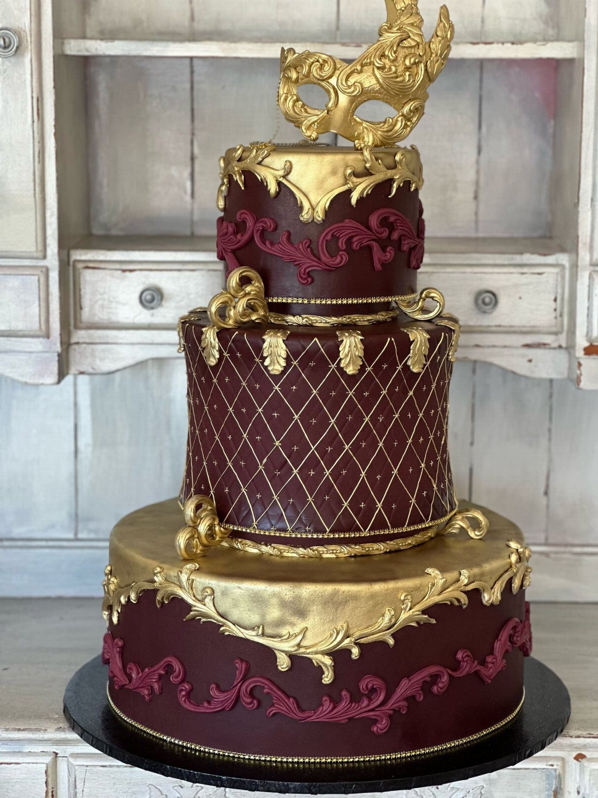 Quince Cake Ideas: 18 Designs From Florals to Butterflies 2 Three-tier burgundy and gold cake topped with a gold masquerade mask.