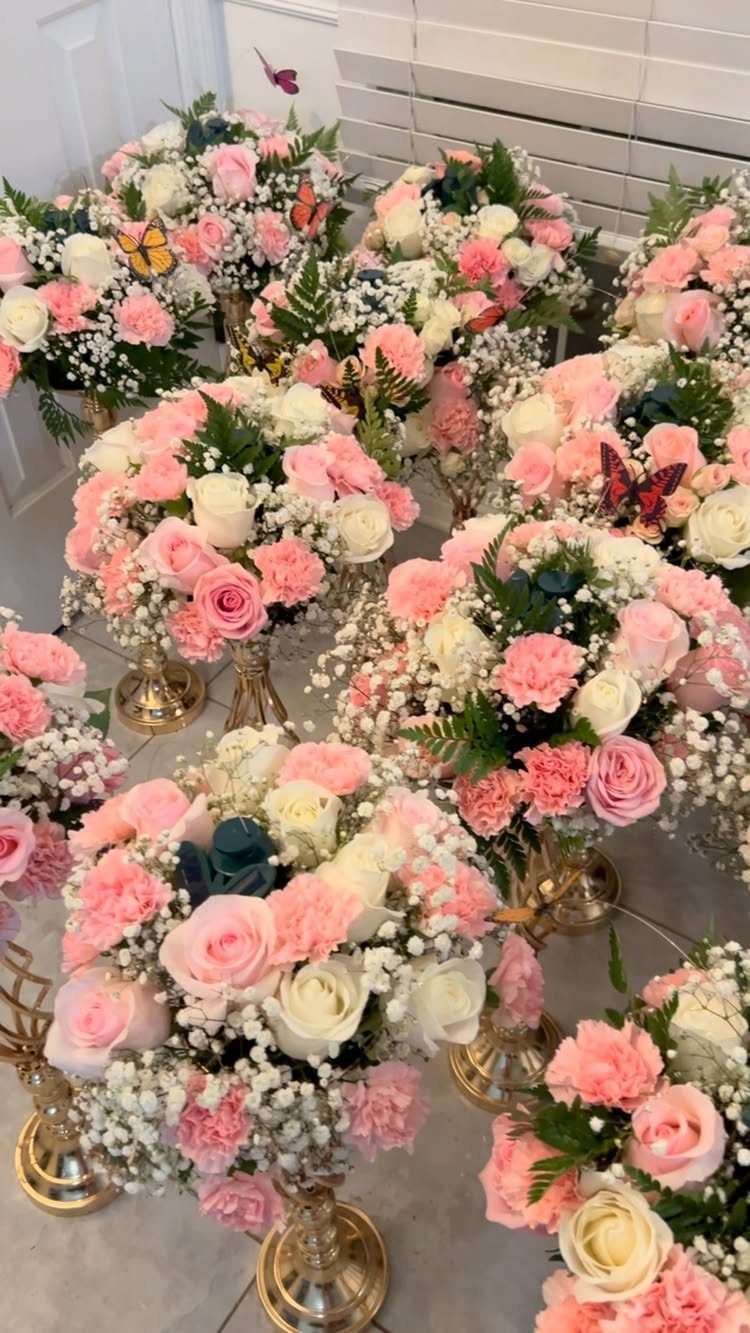 Pink and white rose floral centerpieces in gold vases with colorful butterfly accents.