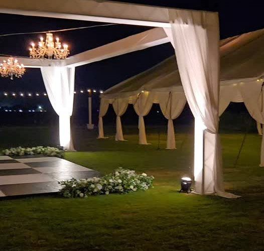Crystal chandeliers hanging from a white canopy over an outdoor event space at night.