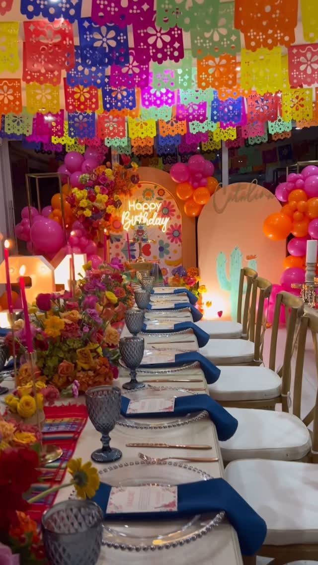 Colorful papel picado banners hanging over a decorated party table with floral arrangements.