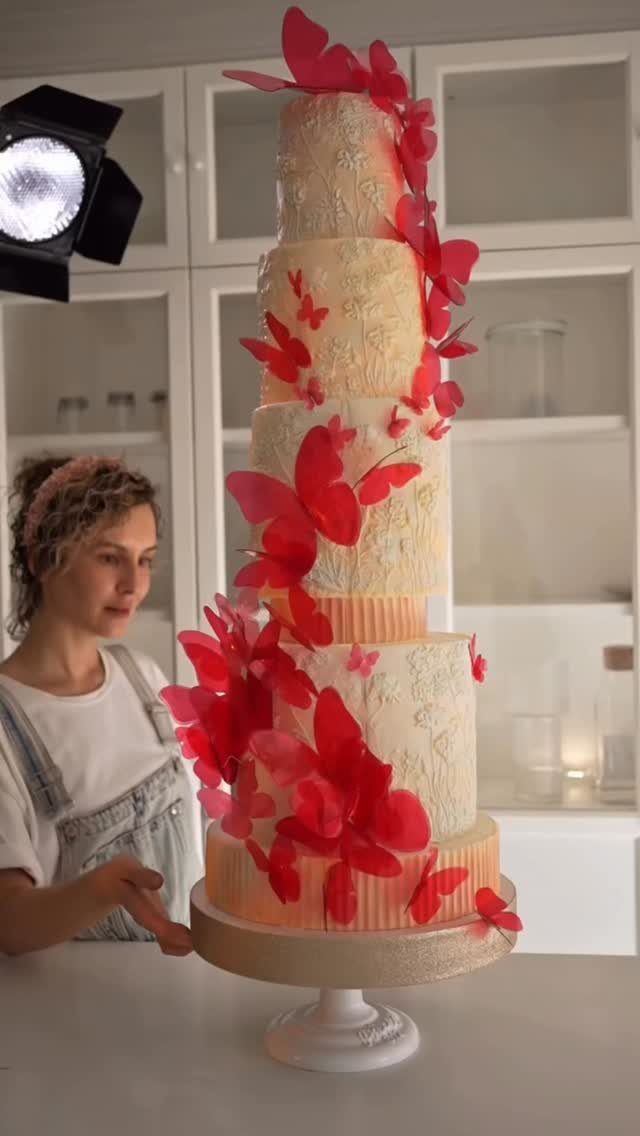 38 Romantic Wedding Cake Ideas for Your Celebration 35 Multi-tiered white wedding cake adorned with vibrant red edible butterflies on a stand.