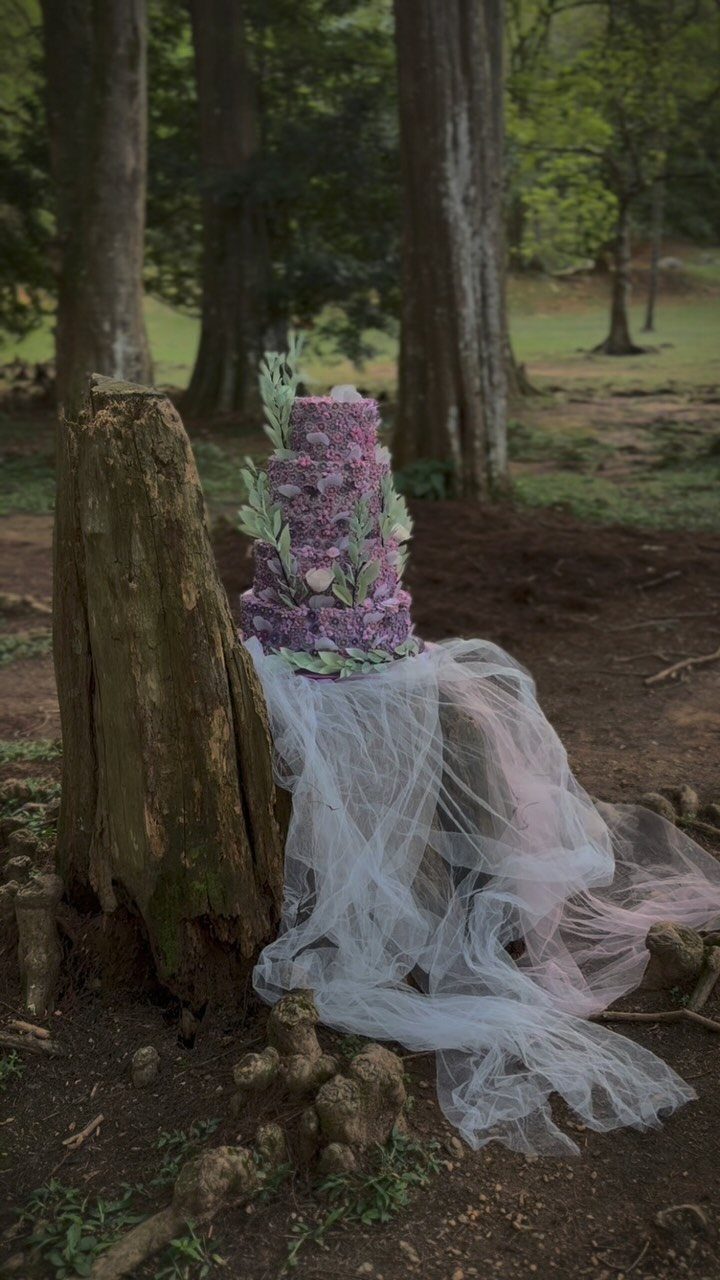 38 Romantic Wedding Cake Ideas for Your Celebration 34 Purple floral tiered cake on a tree stump in a woodland forest setting.