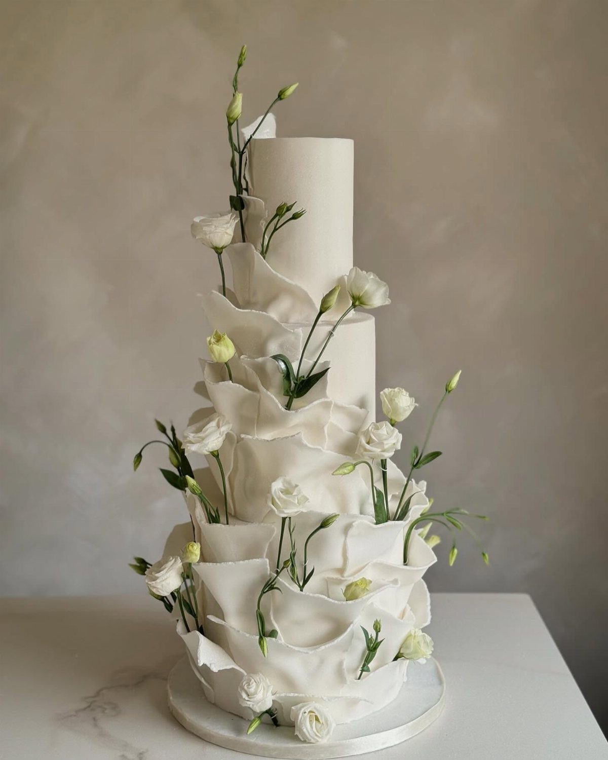 38 Romantic Wedding Cake Ideas for Your Celebration 12 White tiered wedding cake with large fondant ruffles and fresh white lisianthus flowers.
