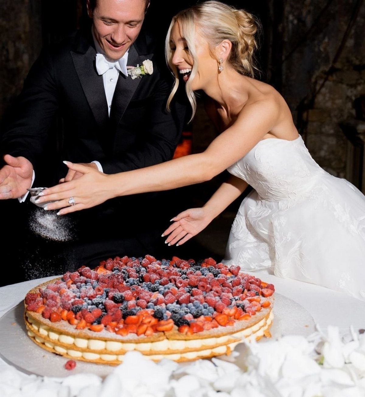 38 Romantic Wedding Cake Ideas for Your Celebration 4 Bride and groom sprinkling powdered sugar on a fresh berry wedding cake.
