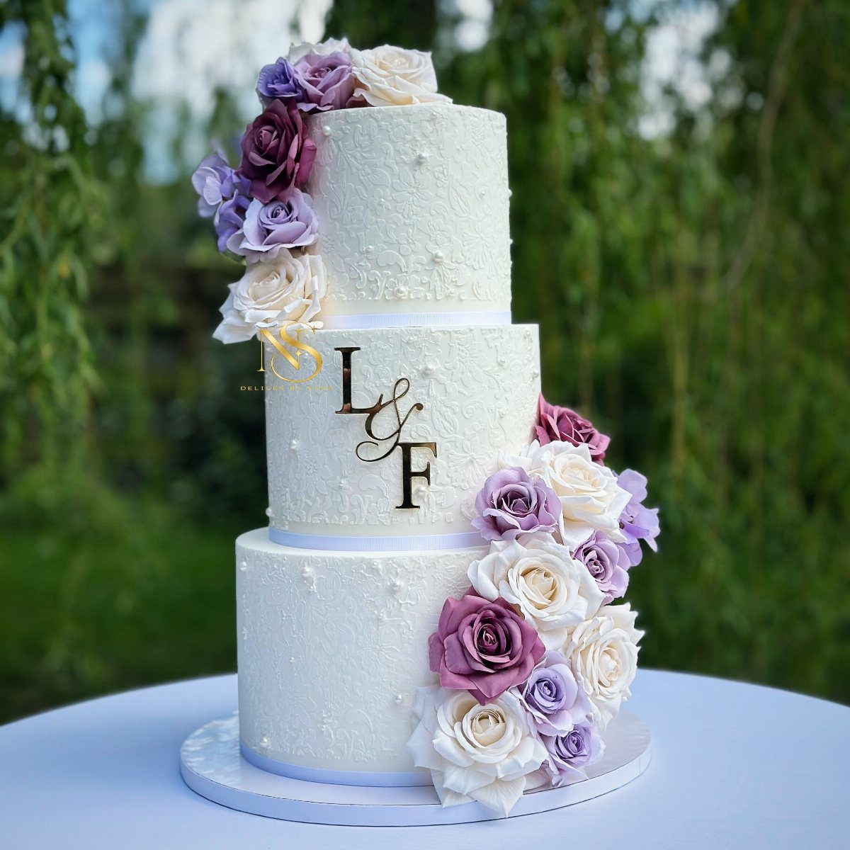 38 Romantic Wedding Cake Ideas for Your Celebration 7 Three-tier white wedding cake decorated with purple and white roses and gold initials.