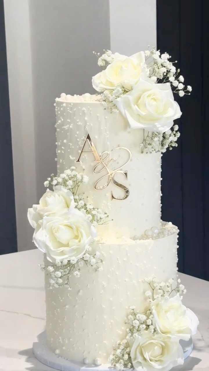38 Romantic Wedding Cake Ideas for Your Celebration 8 Two-tier white wedding cake with gold monogram, white roses, and baby's breath flowers.