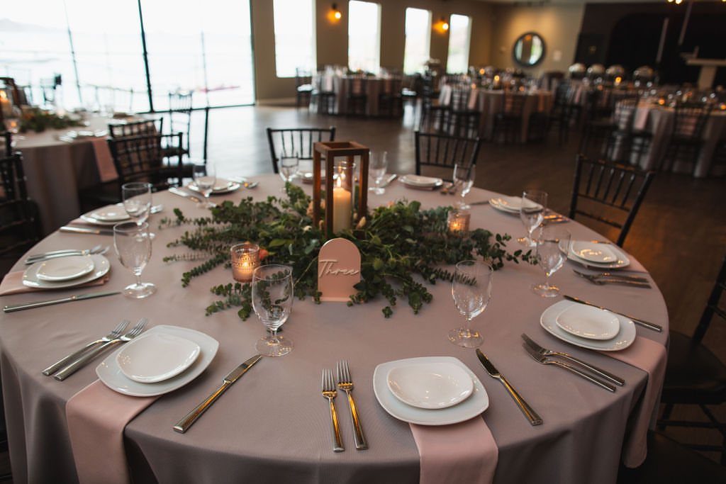 13 Round Table Wedding Decor Ideas: From S-Curved Layouts to Draped Florals 5 A decorated round wedding table featuring a wooden lantern and small candles amidst greenery.