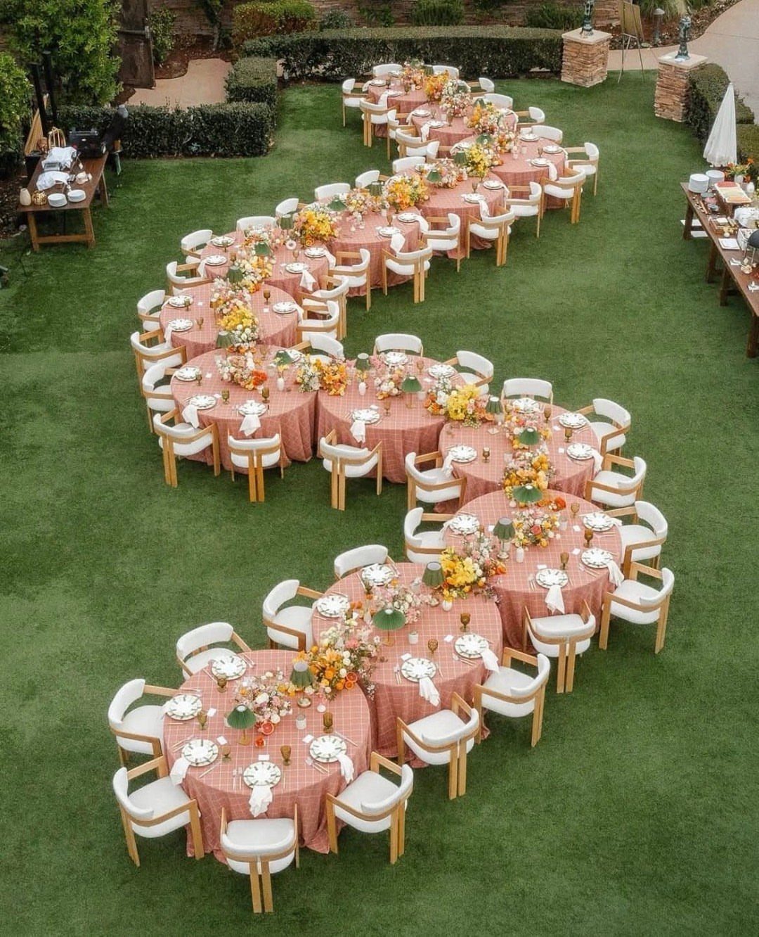 13 Round Table Wedding Decor Ideas: From S-Curved Layouts to Draped Florals 13 Round tables with peach linens and floral centerpieces arranged in an S-curve on a green lawn.