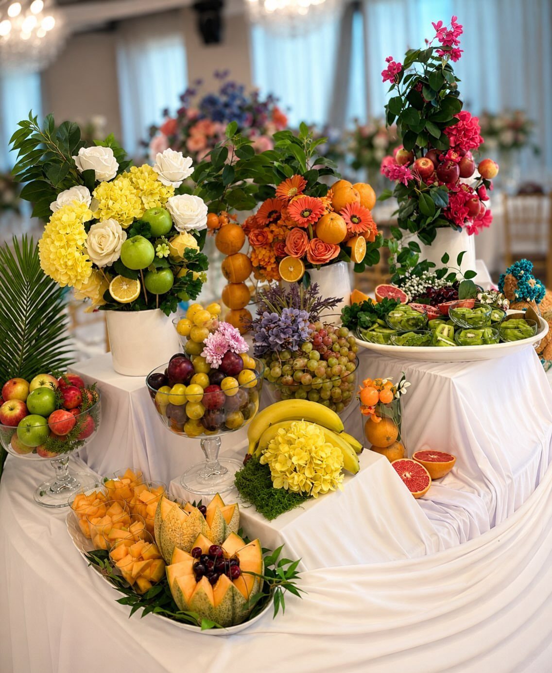 13 Round Table Wedding Decor Ideas: From S-Curved Layouts to Draped Florals 6 A white-clothed buffet table overflowing with assorted fresh fruits and vibrant floral arrangements.