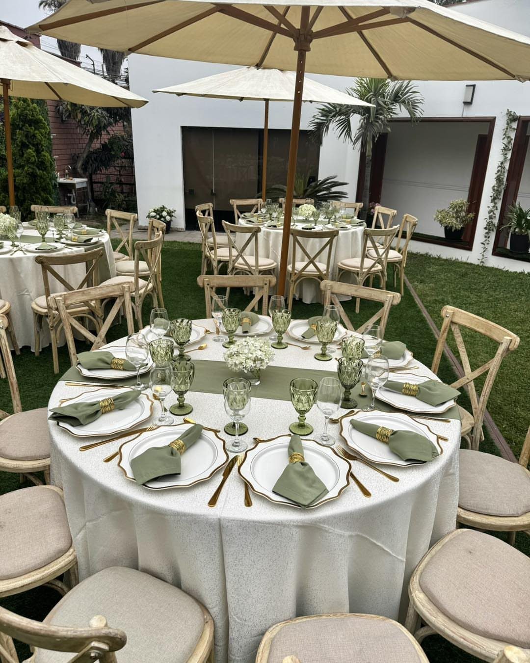 13 Round Table Wedding Decor Ideas: From S-Curved Layouts to Draped Florals 10 A round wedding table set with white linens, green napkins, and gold-rimmed plates outdoors.