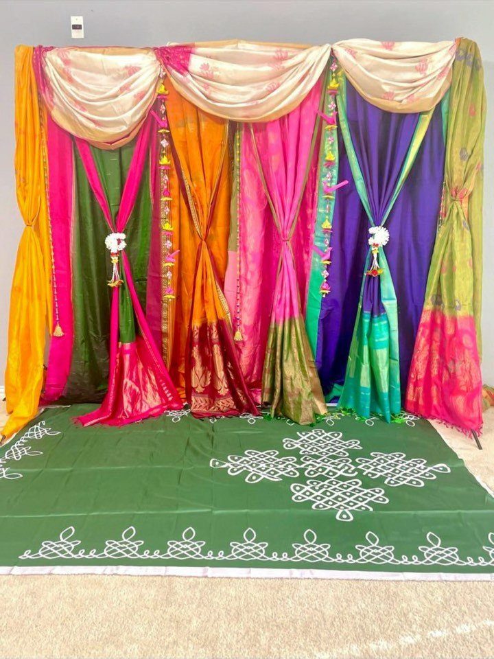 Colorful draped sarees forming a decorative backdrop over a patterned green floor mat.