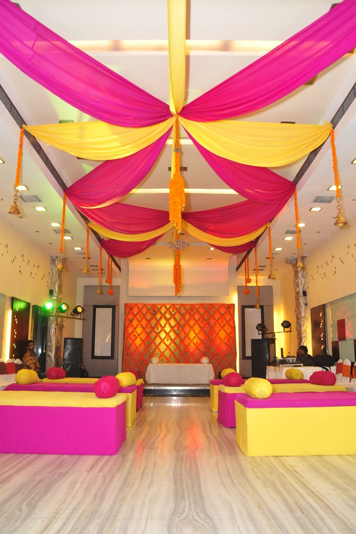 Pink and yellow fabric ceiling drapes in a decorated event hall with marble floors.