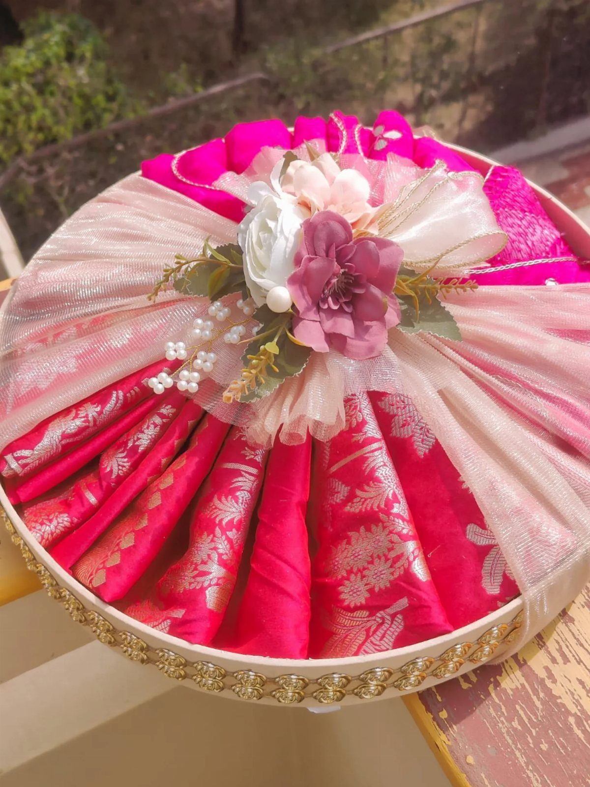 Pink silk saree pleated in a circular gold-rimmed tray with floral decorations