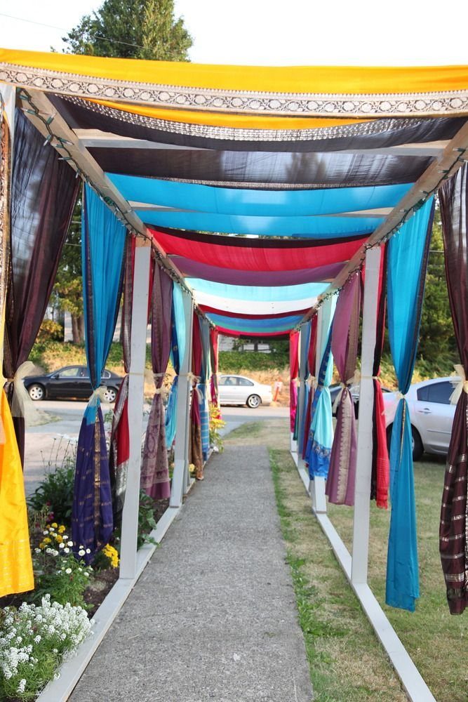 Colorful sarees draped over a white metal frame creating a canopy over a walkway.