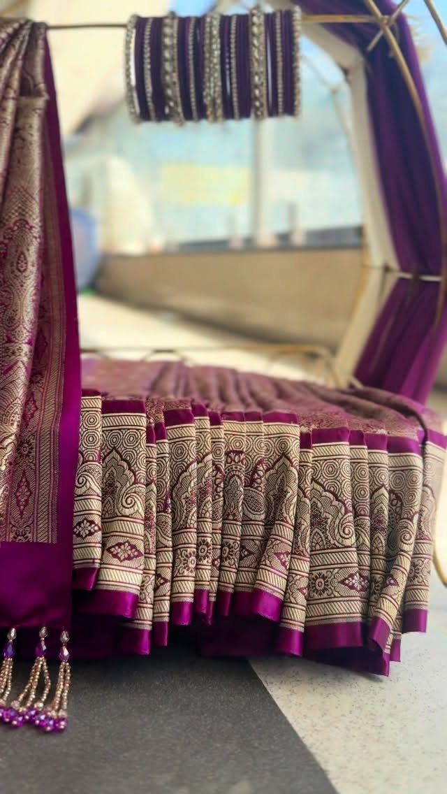 Purple silk saree with gold borders draped over a swing with silver bangles.