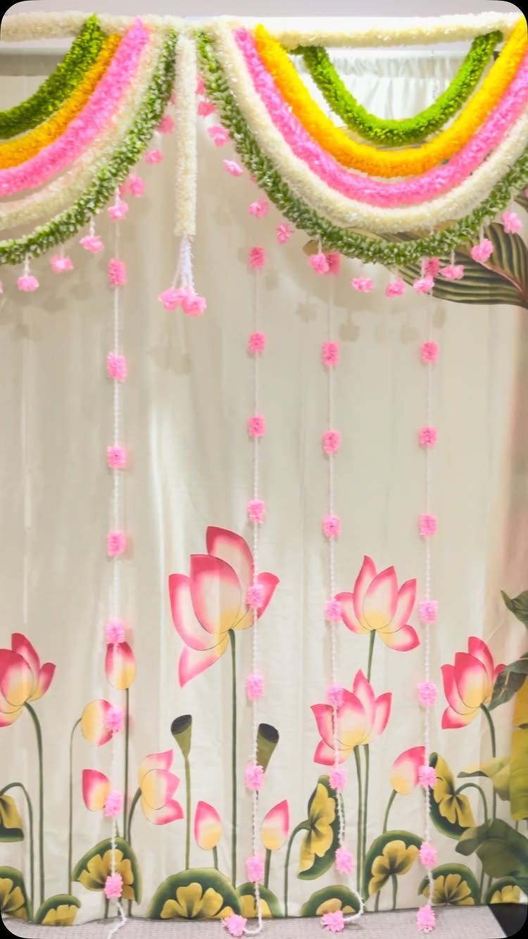 White fabric with lotus prints decorated with colorful floral garlands and hanging blossoms.