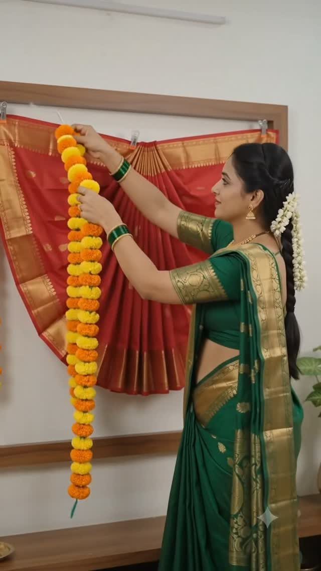 Woman hanging marigold garland in front of a red saree pleated into a fan shape.