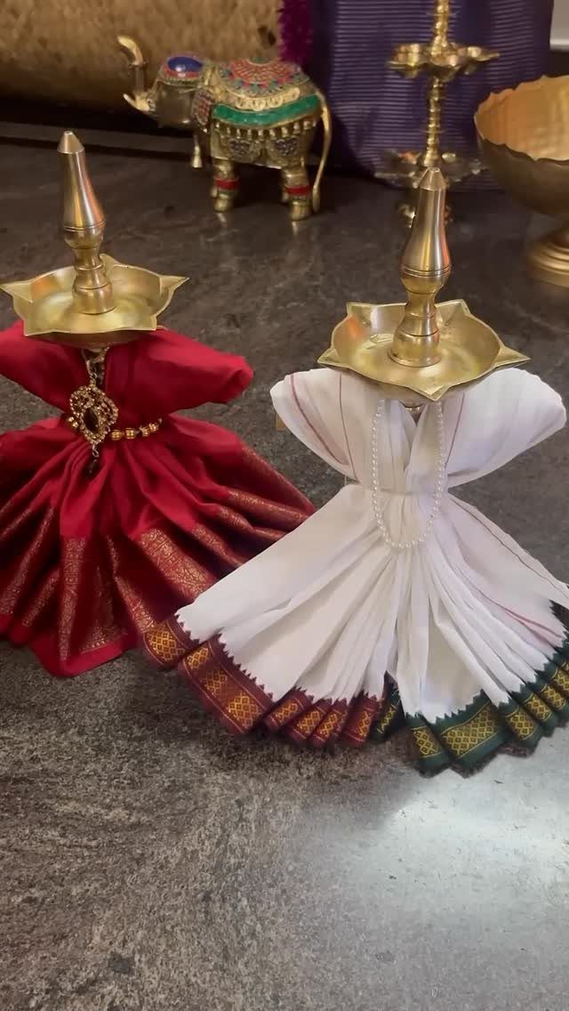 Brass oil lamps resting on red and white sarees draped as small dresses.