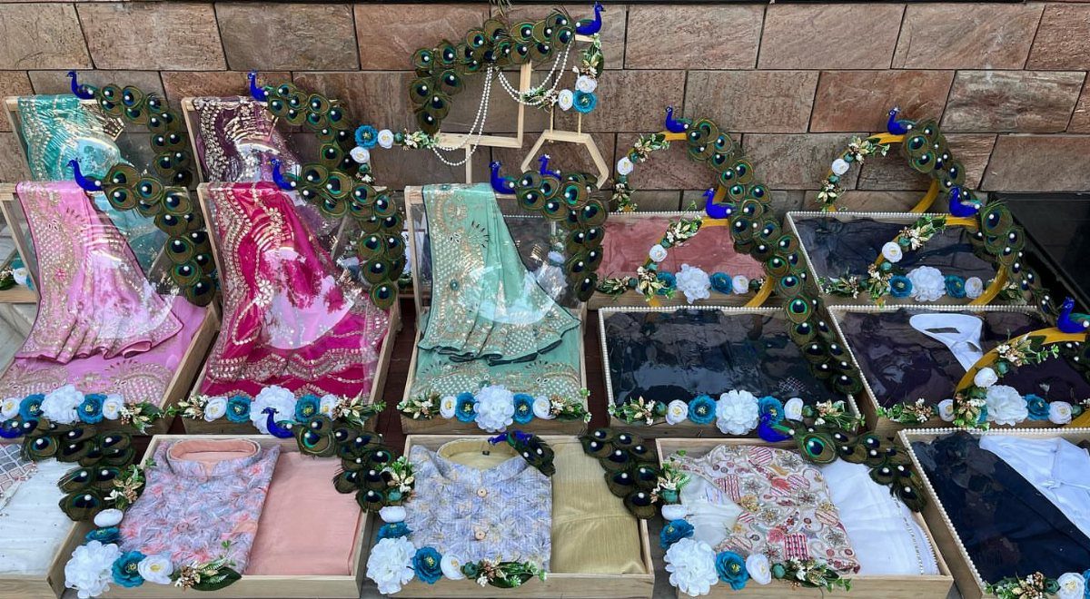 Decorative trays with folded sarees adorned with green beaded peacock feather garlands.
