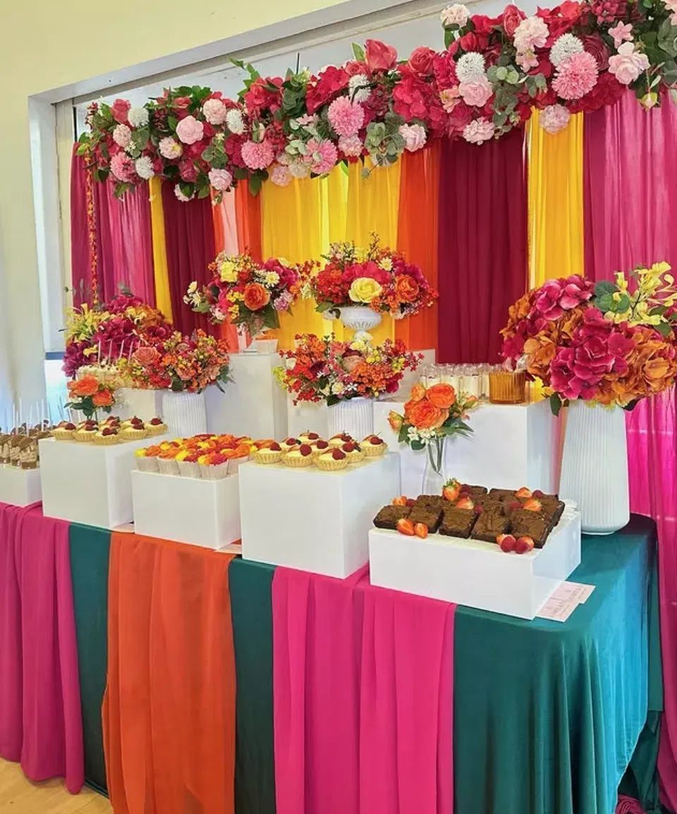 Colorful fabric drapes and floral arrangements decorating a dessert table with sweets.