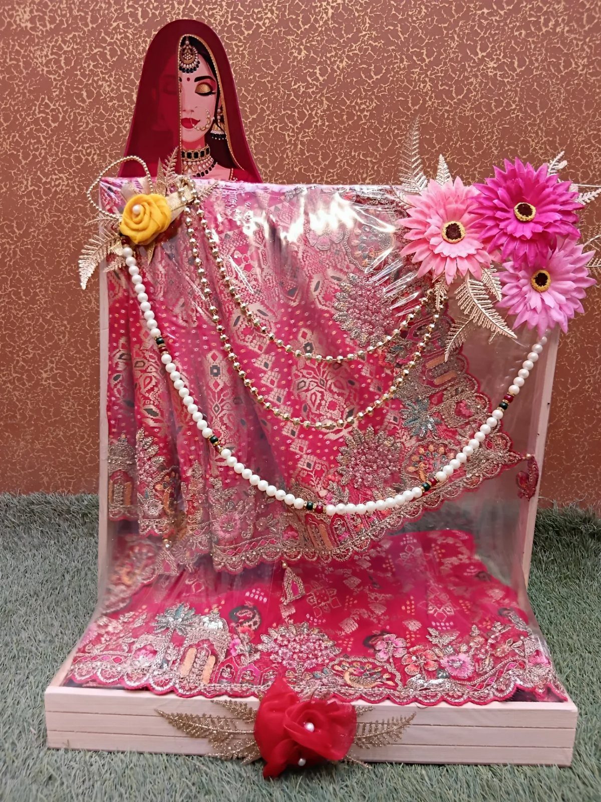 Pink embellished saree displayed in a white tray with pearls and artificial flowers.