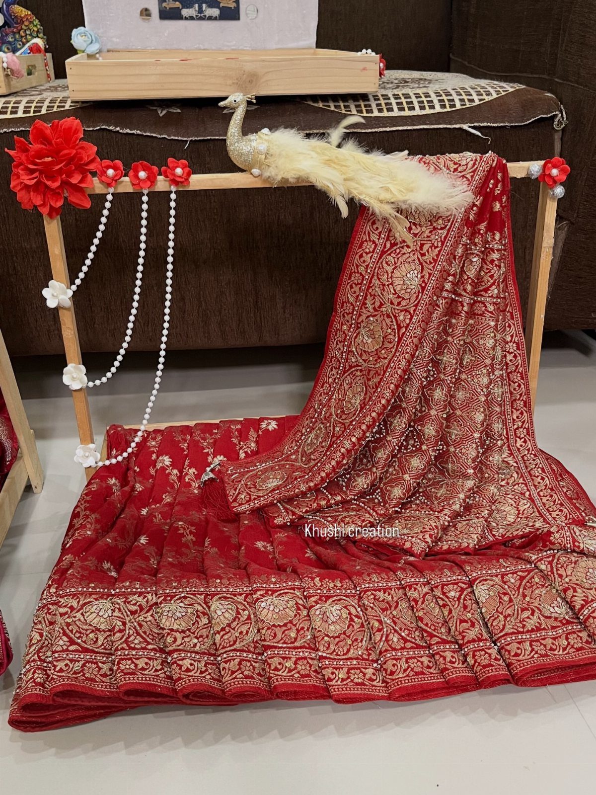 Red silk saree with gold embroidery draped on a decorated wooden frame.