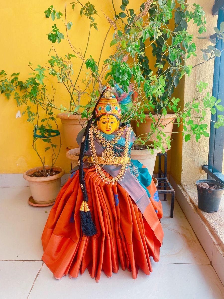 Varalakshmi idol draped in an orange silk saree with gold jewelry and crown.