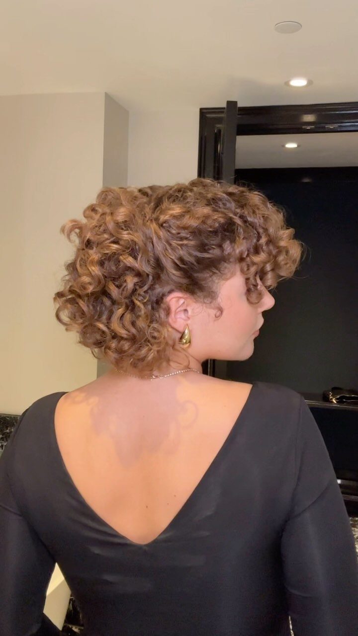 9 Short Curly Hairstyles for Wedding Day Perfection 3 Woman with short voluminous golden-brown curly hair wearing a black V-neck dress.